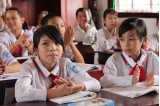 Vietnamesiske skoleelver i skoleuniform sidder ved deres skrivepult og klapper.